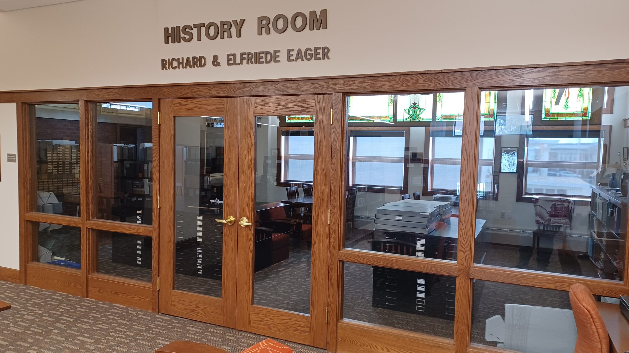 Large room with a wall of windows and french doors.  Many file boxes, flat file drawers, and shelves hold historical resources.
