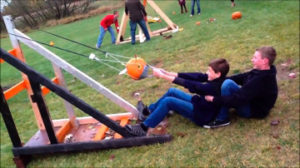 Two teenage boys working together to launch pumpkin in a homemade catapult