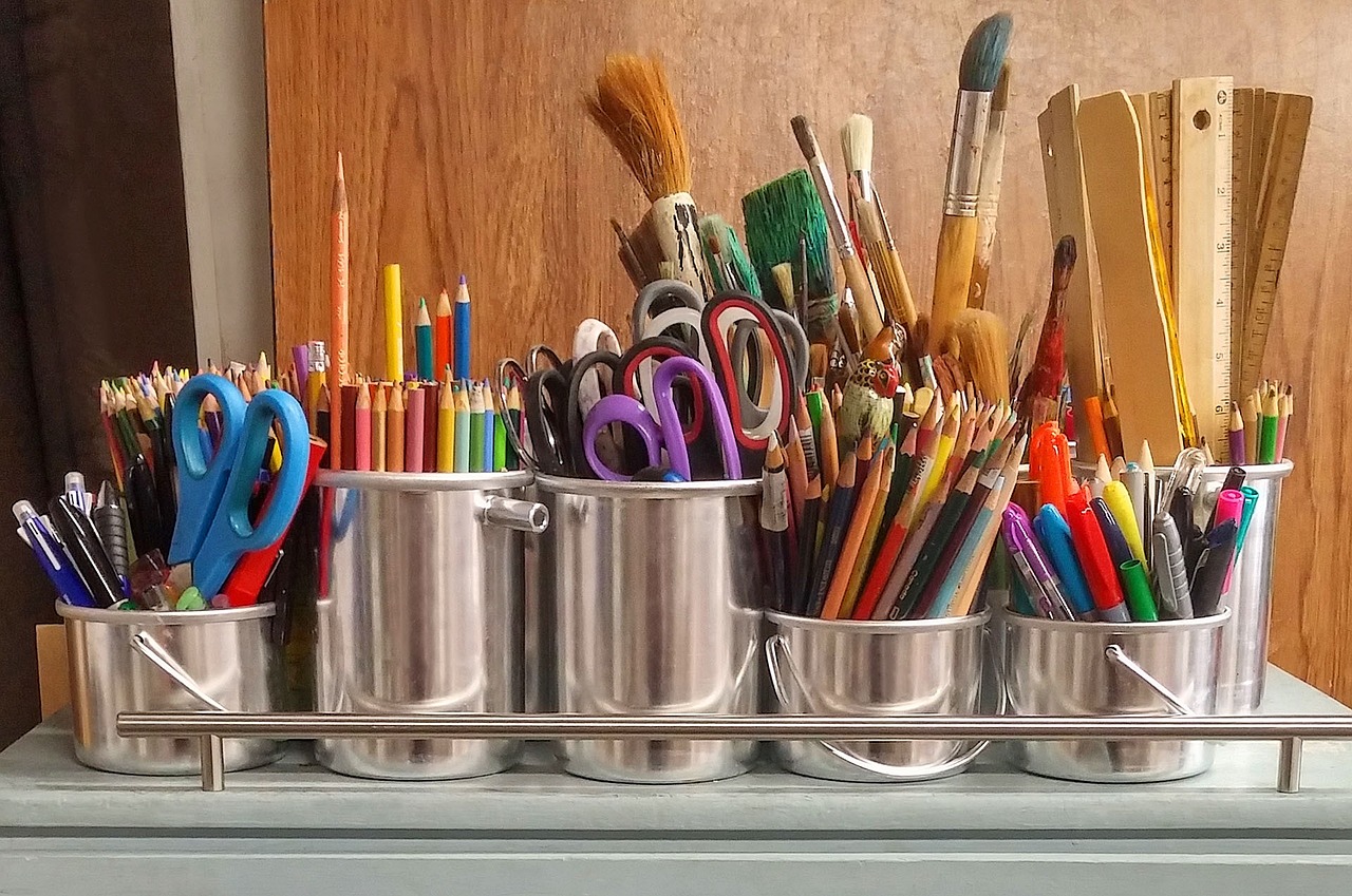 An art caddy with chrome containers full of colored pencils, scissors, rulers, paint brushes, markers and pens.