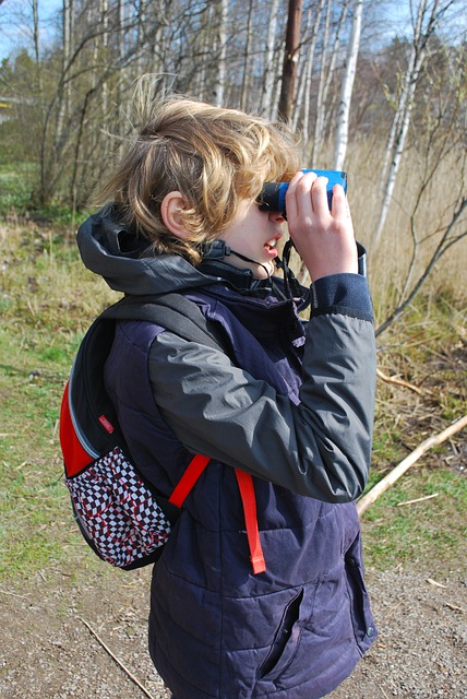 Tween boy looking through binoculars outside.