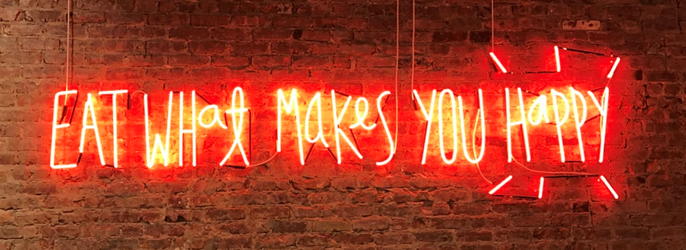 Brick wall with neon red light up words that read Eat What Makes You Happy