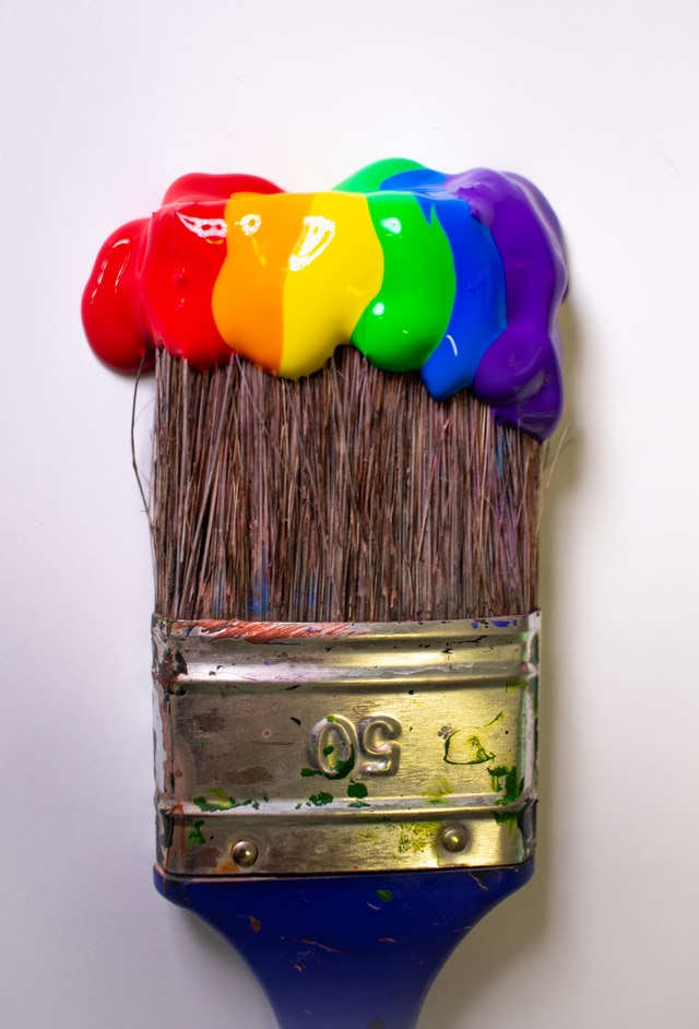Large paintbrush with a rainbow color of paints on it.