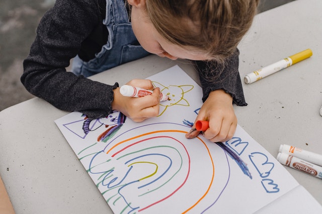 A child using colorful markers to draw a rainbow.
