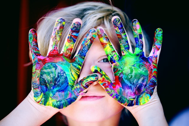 Young child with his hands over his face all covered in colorful paint