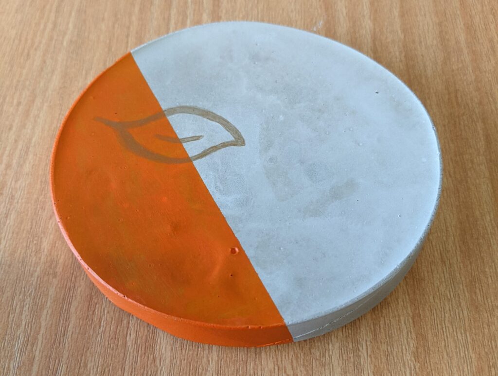 Round cement coaster painted with orange and gold