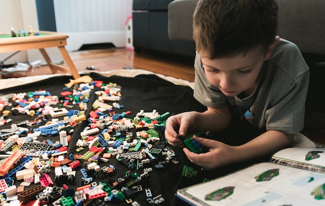 Child laying on the floor with Lego bricks spilled out in front of him while building with Legos.
