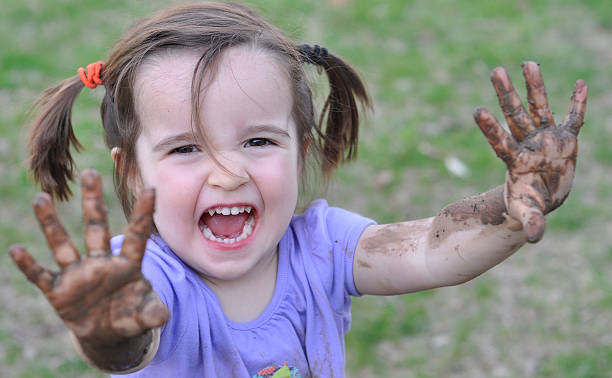 Little girls takes a break from playing to show her muddy hands.