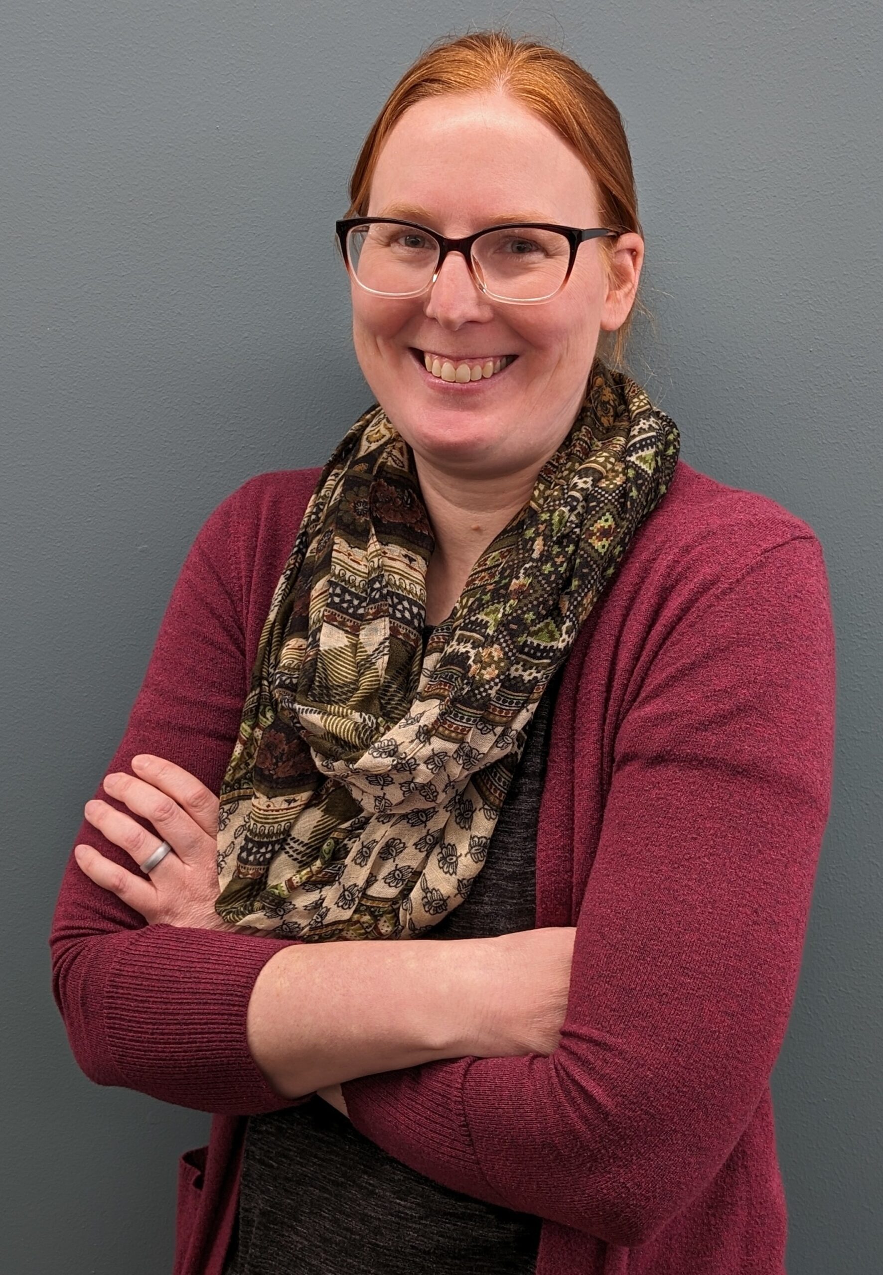 smiling professional picture of Angla in front of a dark grey wall.
