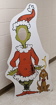Cardboard standup of the illustrated Grinch with his dog Max. Grinch has a cutout for a face.
